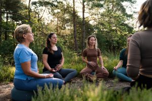 Deelnemers genieten van een rustige yogasessie in de buitenlucht tijdens de Marber Recharge Retraite, omgeven door de serene natuur van de Veluwe.